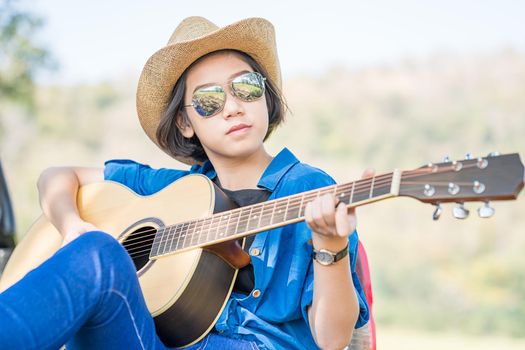 Close up young asian women short hair wear hat and sunglasses playing guitar in countryside Thailand