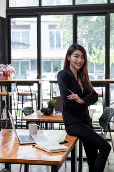 Image of a charming young Asian businesswoman standing at the office with laptop computer of workspace. Looking camera.