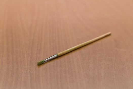 Close-up of an artistic paintbrush lies on the table alone. The subject for painting with paints is ready to work. Wooden brush made of bristles.