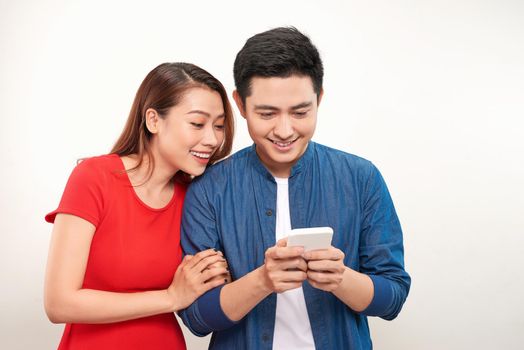 Happy young couple standing behind white background and using their phones