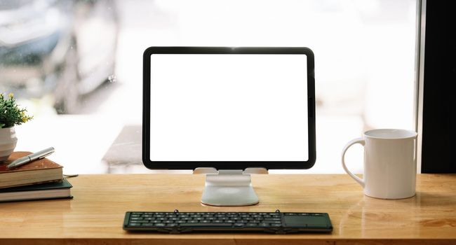 Portable workspace with blank screen tablet on wooden desk with copy space and decorations in coffee shop