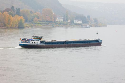 Inland cargo vessel barge on waterway river Rhine with autumn fall colored landscape on shore, North Rhine-Westphalia, Germany, Europe