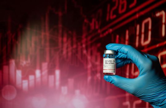 Hands of a researcher in medical gloves holding a Coronavirus Vaccine  with stock index chart background.