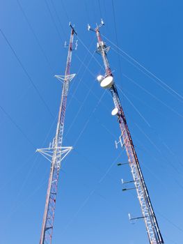 Two metal truss communication towers with various telecommunication antenna equipment, against clear blue sky, shot from low-angle