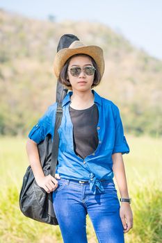 Young asian woman short hair wear hat walking and carry her guitar bag along in countryside Thailand