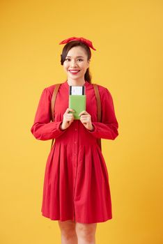 Travel and Lifestyle concept: Full length studio portrait of pretty young student woman holding passport with tickets. Isolated on bright yellow background.