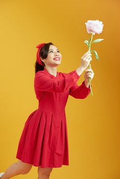 Studio shot of charming woman isolated over yellow studio background, holding white peony flower, having pleased expression. 