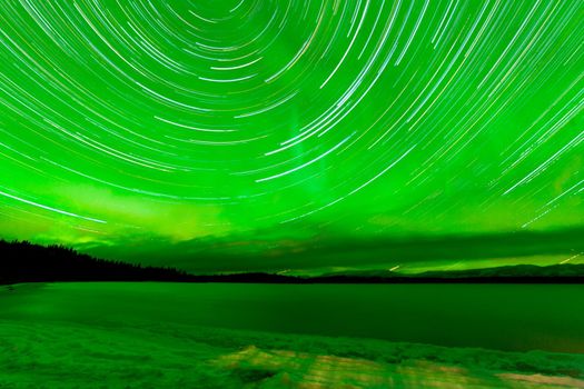 Astrophotography star trails with green sparkling show of Aurora borealis or Northern Lights over boreal forest taiga winter scene of Lake Laberge, Yukon Territory, Canada