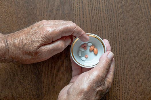 An elderly man holding a cup of pills in his hands selects the desired pill from it