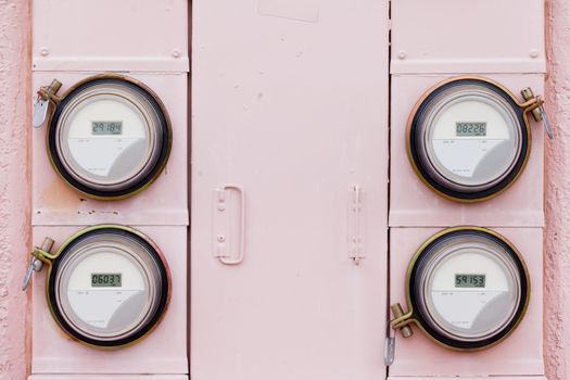 Array of four modern smart grid residential digital power supply watthour meters on grungy pink exterior wall