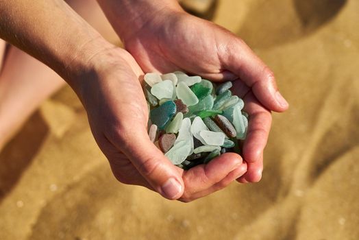 A pile of various colours of sea glass are held by two hands