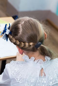 A girl's hairstyle with a braid around her head and a blue bow close-up. Hair styling is done with hairpins and an elastic band. Only the back of the head with a haircut.