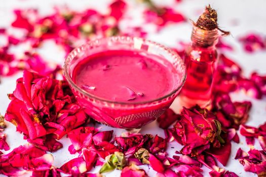 Rose Jam in a glass bowl with some essential oil or concentration of rose in a glass bottle along with some rose petals spread on the surface.