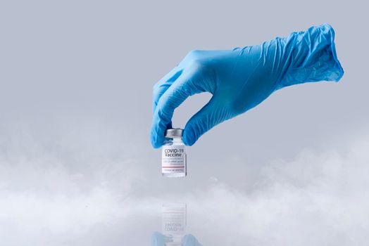 Hand holding frozen cold Vaccine vial for Covid-19. Isolated and smoke in Lab theme.
