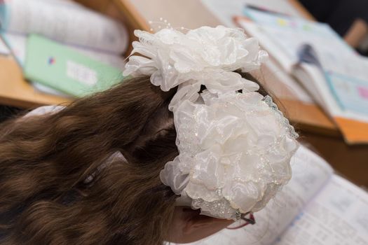 A close-up of a girl's hairstyle with fluffy hair and two white bows. Hair styling is done with hairpins and an elastic band. Only the back of the head with a haircut.