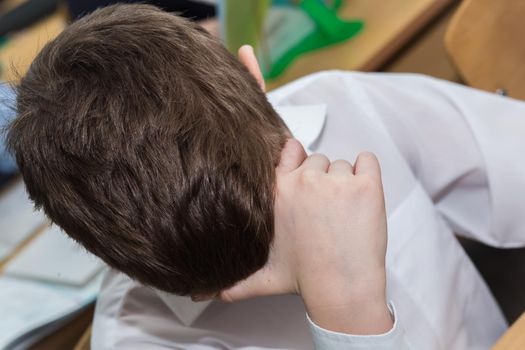 Close-up of a boy's hand supporting his head. A student at school sits at a desk and thinks or sleeps in class. Top view of the head of a man with a short haircut.