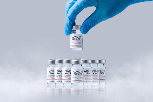 Hand holding frozen cold Vaccine vials for Covid-19 vaccine in laboratory. Group of Coronavirus vaccine bottles.