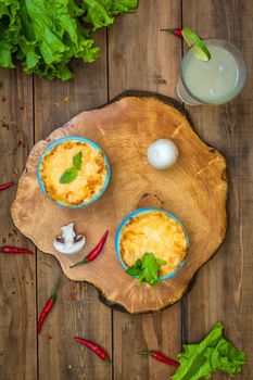 Pots with mushroom julienne on a wooden board, decorated with herbs. Julienne in cocotte with yellow cheese crust. View from above.