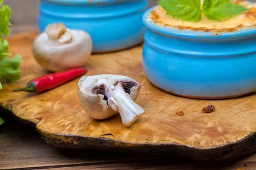 A pot of mushroom julienne on a wooden board, decorated with herbs. Julienne in cocotte with yellow cheese crust. Close-up.