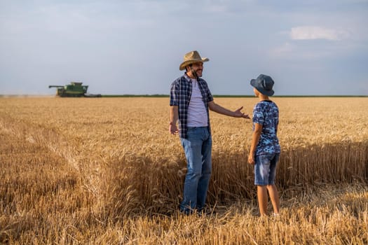 Farmers are standing in their wheat field while the harvesting is taking place. Father is teaching his son about agriculture.