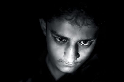 Portrait shot of young white isolated on black wearing black colored shirt and expressing angriness and mysteriousness on his face.