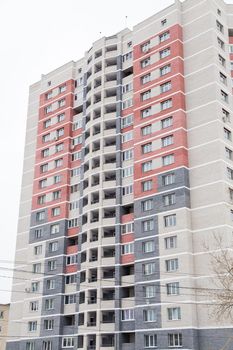 Residential high-rise building in a new residential area of the city. Against the background of the gray sky. Modern new buildings, building facades. Real estate and urban architecture concept.