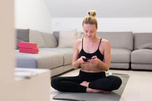 Beautiful blonde woman doing home workout indoors. Woman practice yoga at home. Fit girl using workout tutorials for healthy active lifestyle. Woman using quarantine for home workouts. Stretching