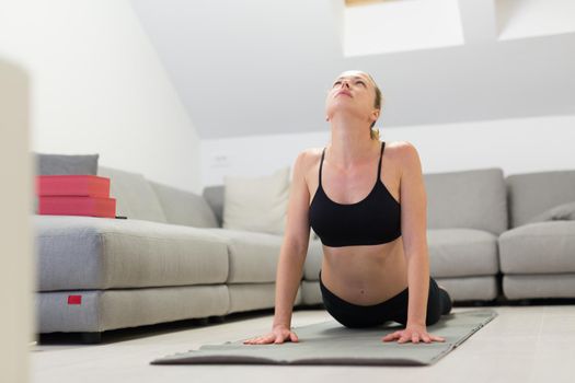 Beautiful blonde woman doing home workout indoors. Woman practice yoga at home. Fit girl using workout tutorials for healthy active lifestyle. Woman using quarantine for home workouts. Stretching