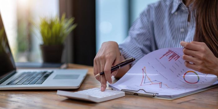 Close up Business woman using calculator and laptop for do math finance on wooden desk in office and business working background, tax, accounting, statistics and analytic research concept.