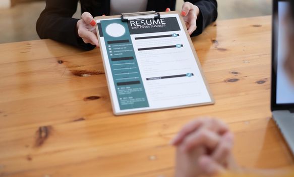 Close up people hands on a wooden table, boss and woman during interview. Director hr manager holding resume paper, woman talking about yourself. HR recruitment and hiring concept.