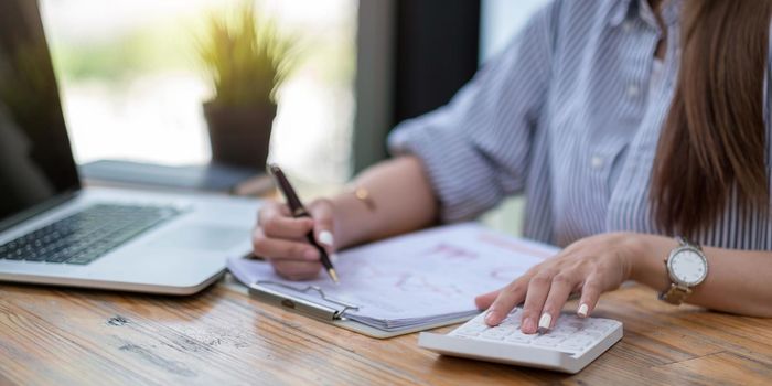 Close up Business woman using calculator and laptop for do math finance on wooden desk in office and business working background, tax, accounting, statistics and analytic research concept.