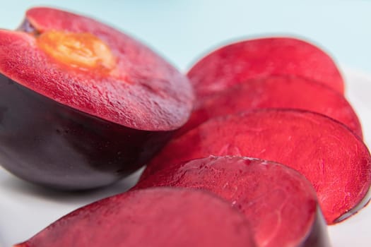 On a white saucer, a large plum, cut in half, with slices next to it. The pulp of red berries. Close-up.