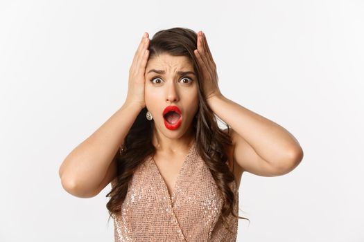 Concept of New Year celebration and winter holidays. Close-up of woman in luxury dress looking shocked and worried, standing over white background.