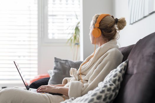 Stay at home, shelter in place and social distancing. Woman in her casual home bathrobe relaxing while working remotly from her living room. Using social media apps for video chatting.