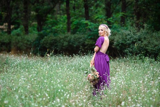 Girl model blonde in a lilac dress with a bouquet with a green forest