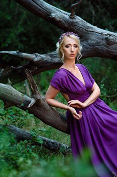 Girl model blonde in a lilac dress with a bouquet with a green forest