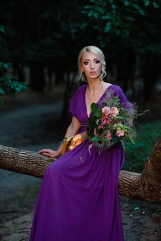 Girl model blonde in a lilac dress with a bouquet with a green forest