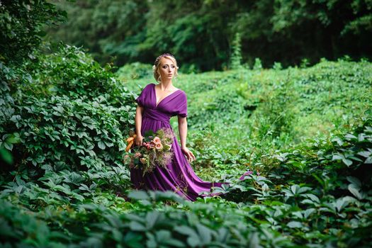 Girl model blonde in a lilac dress with a bouquet with a green forest