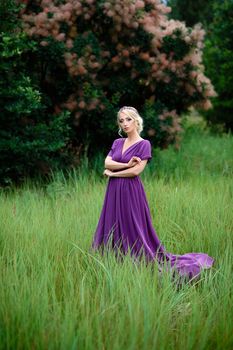 Girl model blonde in a lilac dress with a bouquet with a green forest