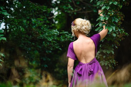 Girl model blonde in a lilac dress with a bouquet with a green forest