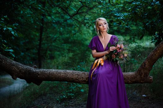 Girl model blonde in a lilac dress with a bouquet with a green forest