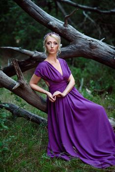 Girl model blonde in a lilac dress with a bouquet with a green forest