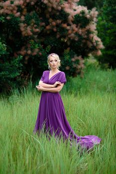 Girl model blonde in a lilac dress with a bouquet with a green forest