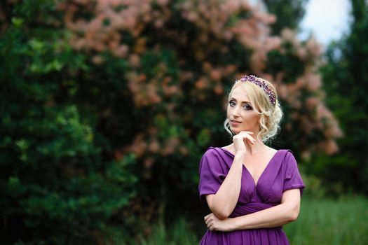 Girl model blonde in a lilac dress with a bouquet with a green forest