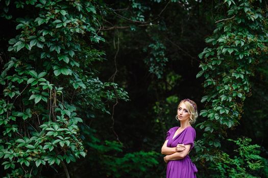 Girl model blonde in a lilac dress with a bouquet with a green forest