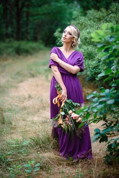 Girl model blonde in a lilac dress with a bouquet with a green forest