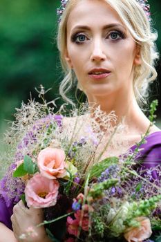 Girl model blonde in a lilac dress with a bouquet with a green forest