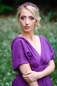 Girl model blonde in a lilac dress with a bouquet with a green forest