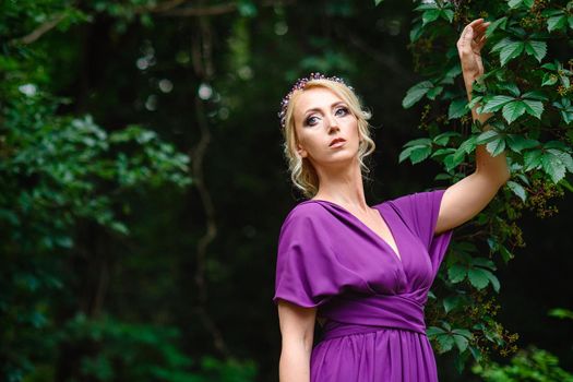 Girl model blonde in a lilac dress with a bouquet with a green forest