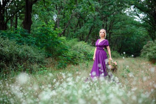 Girl model blonde in a lilac dress with a bouquet with a green forest